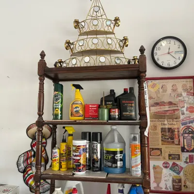 Sale Photo Thumbnail #244: Four-tier dark wood shelving unit filled with household chemicals, motor oil, and cleaning supplies, topped with an ornate gold wire shelf.