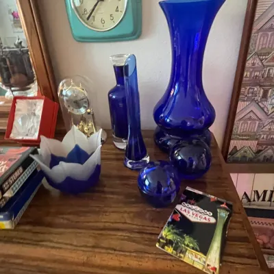 Sale Photo Thumbnail #99: Collection of cobalt blue glassware, including a large flared vase, bud vase, decanter, and paperweights, displayed alongside a turquoise wall clock.