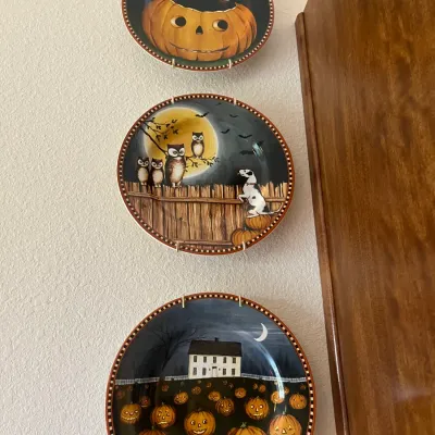 Sale Photo Thumbnail #142: Trio of decorative Halloween-themed wall plates mounted on plate hangers, featuring folk art illustrations of pumpkins, a black cat, owls, and a dog.