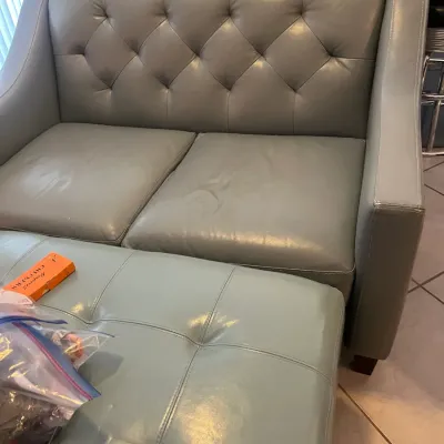 Sale Photo Thumbnail #46: Contemporary grey leather loveseat with a diamond-tufted backrest and matching tufted ottoman, showing minor wear.