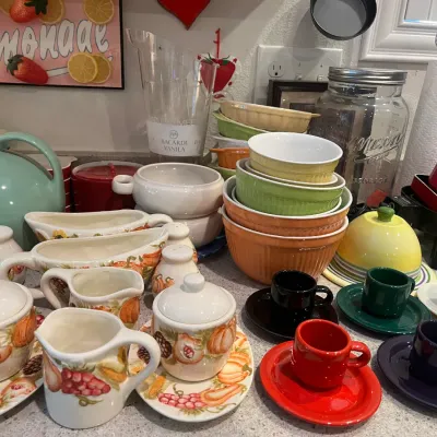 Sale Photo Thumbnail #23: Collection of kitchenware and tableware, including Fiesta espresso cups and saucers, ceramic ramekins, a Fiesta disc pitcher, and fruit-patterned creamer and sugar sets.