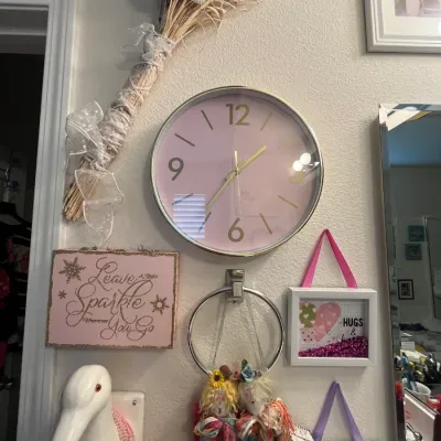 Sale Photo Thumbnail #127: A wall display featuring a modern pink round wall clock with gold numbers, surrounded by decorative signs, a broom accent, a duck head figurine wearing beads, and hanging artwork.