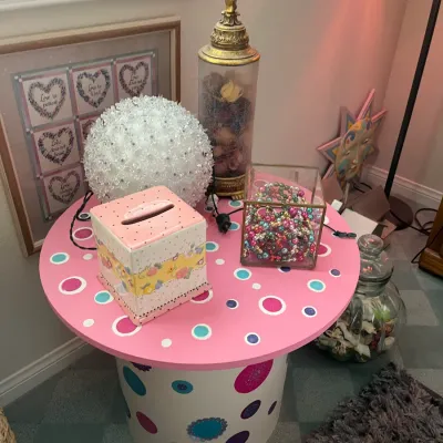 Sale Photo Thumbnail #196: Whimsical pink and white polka-dot accent table holding decorative accessories, including a tissue box cover, glass jar with potpourri, and a glass display box.