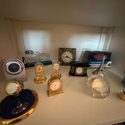 Sale Photo Thumbnail #116: Collection of decorative table clocks and novelties, including brass anniversary clocks, a crystal desk clock, and a miniature toilet-shaped clock.