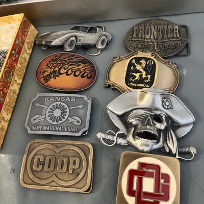 Sale Photo Thumbnail #53: Collection of vintage novelty and promotional belt buckles featuring designs including Coors, Löwenbräu, Frontier Hotel Las Vegas, Kansas Army National Guard, a Corvette, and a pirate skull.