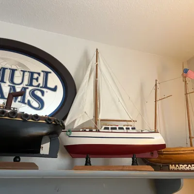 Sale Photo Thumbnail #210: Collection of detailed wooden model ships, including a sailboat, a tugboat, and the 'Margaret' schooner, displayed alongside a framed Samuel Adams beer sign.