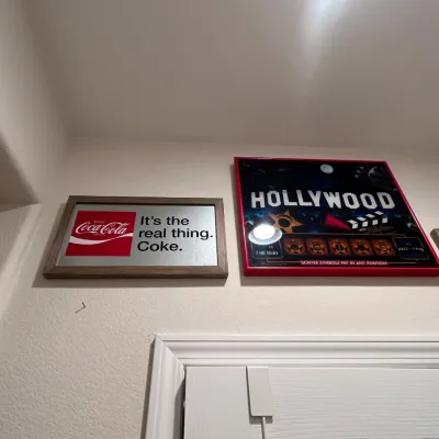 Sale Photo Thumbnail #67: Framed wall art featuring a mirrored Coca-Cola advertisement sign alongside a red-framed Hollywood-themed slot machine glass panel.