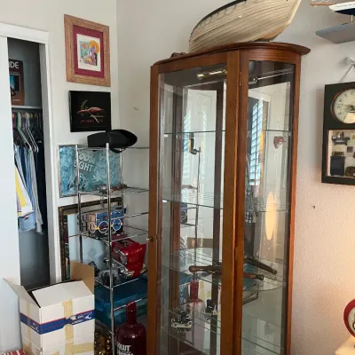Sale Photo Thumbnail #212: Tall oak display cabinet with glass shelves, housing various collectibles alongside a model sailboat displayed on top.