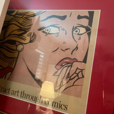 Sale Photo Thumbnail #225: Framed pop art exhibition poster featuring Roy Lichtenstein's 'Crying Girl' style artwork, matted in red with a gold-tone metal frame.