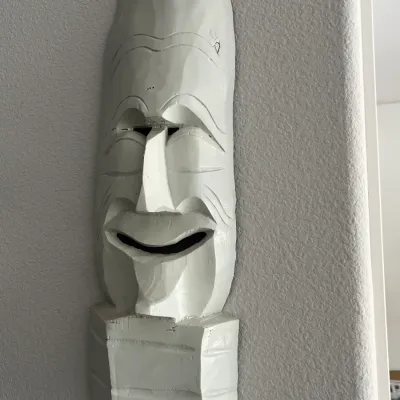 Sale Photo Thumbnail #252: Hand-carved white-painted wooden mask, styled after a traditional Korean Hahoe mask, featuring a prominent forehead, cheerful expression, and pointed chin, mounted on a wall.