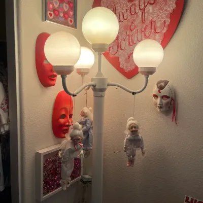 Sale Photo Thumbnail #231: Retro white four-globe floor lamp surrounded by decorative wall masks, framed heart art, and hanging elf figurines.