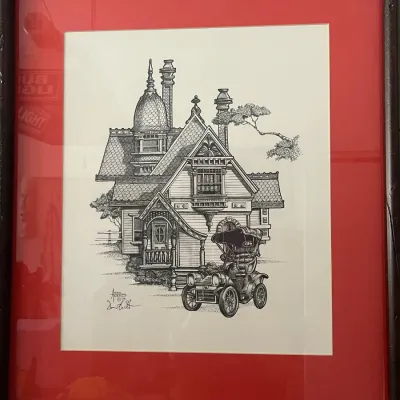Sale Photo Thumbnail #256: Framed black and white pen and ink illustration of a Victorian house and antique car, signed by the artist and dated 1978, presented in a red mat and dark wood frame.