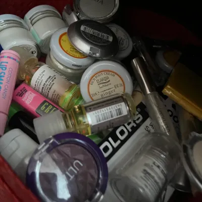 Sale Photo Thumbnail #194: Collection of assorted modern cosmetics and skincare items, including Ulta eyeshadows, Lip Smacker lip balm, and body creams, gathered in a red basket.