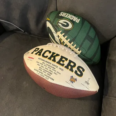 Sale Photo Thumbnail #56: Pair of Green Bay Packers footballs, including a commemorative white panel championship history ball and a green team-branded ball.