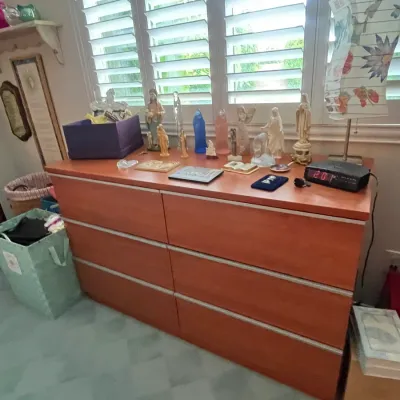 Sale Photo Thumbnail #108: Modern six-drawer wooden dresser topped with religious figurines, a digital alarm clock, and decorative accessories.