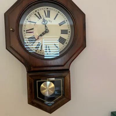 Sale Photo Thumbnail #235: Bulova schoolhouse-style pendulum wall clock in a dark wood case, featuring Roman numerals.