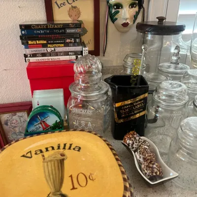 Sale Photo Thumbnail #16: Collection of home decor and kitchen items, including a retro 'Vanilla Shake' ceramic plate set, clear glass storage jars, DVDs, a Johnnie Walker water pitcher, and a ceramic mask wall hanging.