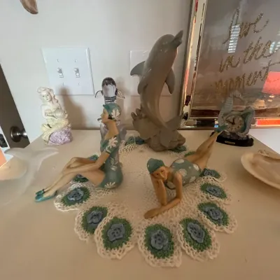 Sale Photo Thumbnail #115: Collection of aquatic and coastal-themed decor items, including bathing beauty figurines, a dolphin statue, a mermaid figurine, and a seahorse desk clock.