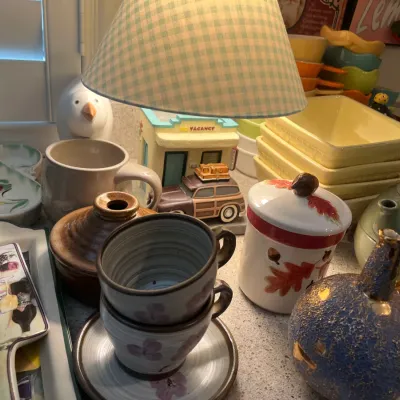 Sale Photo Thumbnail #19: Collection of vintage kitchenware and decor, including ceramic mugs, a small motel-themed cookie jar or figure, an autumn-themed canister, and colorful baking dishes.