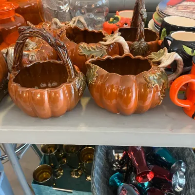 Sale Photo Thumbnail #11: Collection of autumn and Halloween tableware including ceramic pumpkin baskets, pitchers, and themed mugs displayed on a folding table.