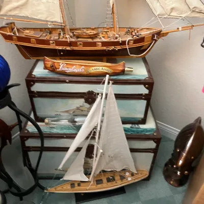 Sale Photo Thumbnail #202: Collection of nautical decor including two wooden sailboat models, stacked painted trunks, and a Leinenkugel's beer tap handle.