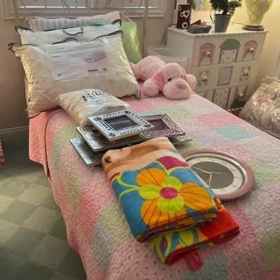Sale Photo Thumbnail #239: White metal twin bed frame displayed with a collection of bedroom items including a pastel patchwork quilt, pillows, picture frames, a wall clock, and a plush pink dog.