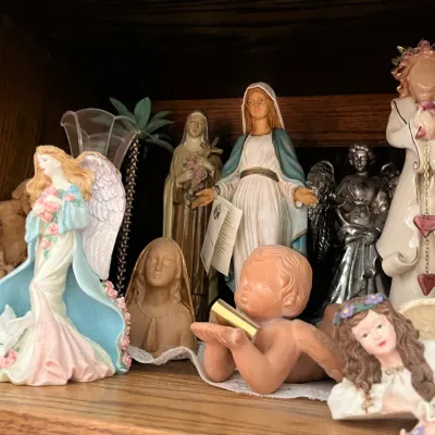 Sale Photo Thumbnail #186: Collection of religious figurines, including Virgin Mary statues, winged angels, and terracotta cherubs displayed on a wooden shelf.