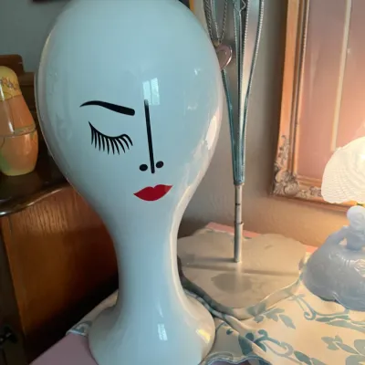 Sale Photo Thumbnail #191: Vintage white ceramic mannequin head with pop-art style face features, including a winking eye and red lips.