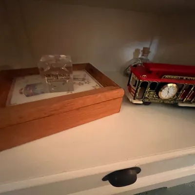 Sale Photo Thumbnail #117: Collection of shelf collectibles featuring a wooden box, clear crystal paperweight, and a vintage red San Francisco Powell & Hyde Sts cable car clock.
