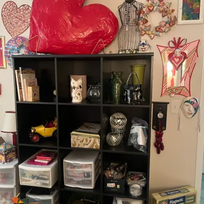 Sale Photo Thumbnail #222: Black 12-cube shelving unit filled with various home decor items, craft supplies, and collectibles, topped with a oversized red heart sculpture and wire dress form.