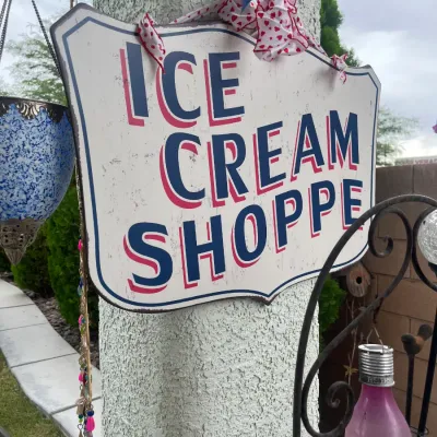 Sale Photo Thumbnail #144: Vintage-style painted metal "Ice Cream Shoppe" sign mounted on a textured post, decorated with a heart-pattern ribbon.