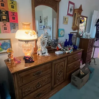 Sale Photo Thumbnail #104: Vintage carved oak triple dresser with matching mirror, topped with a hurricane-style lamp, decorative clocks, and glassware.
