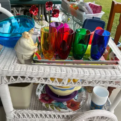 Sale Photo Thumbnail #143: White wicker rolling bar cart featuring a set of colorful jewel-toned drinking glasses on a floral tray, alongside various kitchenware and serving items.