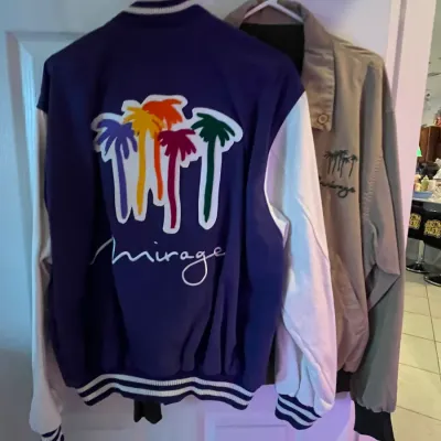 Sale Photo Thumbnail #94: Vintage The Mirage Hotel and Casino satin varsity-style jacket featuring colorful embroidered palm trees and white sleeves, displayed alongside a beige jacket.