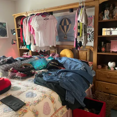 Sale Photo Thumbnail #188: A large assortment of women's clothing, denim, and accessories laid out on a bed, set in front of a wooden Pier 1 style headboard wall unit with shelving.