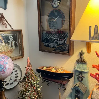 Sale Photo Thumbnail #207: Framed Corvette clock displaying a black C3 Corvette and emblem, alongside various nautical decor items including a wooden speed boat model and lighthouse figurine.