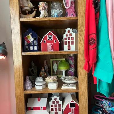 Sale Photo Thumbnail #197: Wooden bookcase filled with home decor, including decorative miniature houses, figurines, trinket boxes, and glassware.