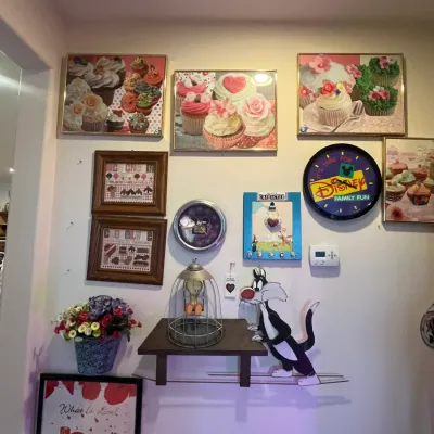 Sale Photo Thumbnail #93: A collection of wall decor featuring framed cupcake artwork, a Disney wall clock, cross-stitch samplers, and Looney Tunes Tweety and Sylvester novelty items.