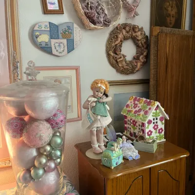 Sale Photo Thumbnail #193: Collection of shabby chic home decor items, including a porcelain doll, floral ceramic cottage, large apothecary jar filled with pink and green ornaments, and heart-themed wall art.