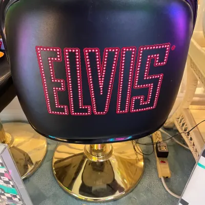 Sale Photo Thumbnail #153: Black vinyl swivel chair featuring a red stud-detailed "ELVIS" logo across the back seat, set on a polished brass dome base.