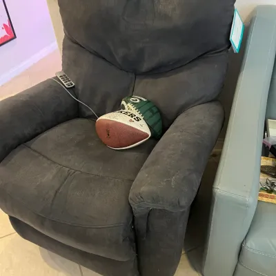 Sale Photo Thumbnail #55: Contemporary dark gray upholstered power recliner with attached remote control, holding a Green Bay Packers commemorative football.