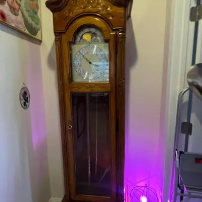 Sale Photo Thumbnail #92: Traditional oak grandfather clock featuring a bonnet top with shell carving, a moon phase dial, and a glass pendulum display door.