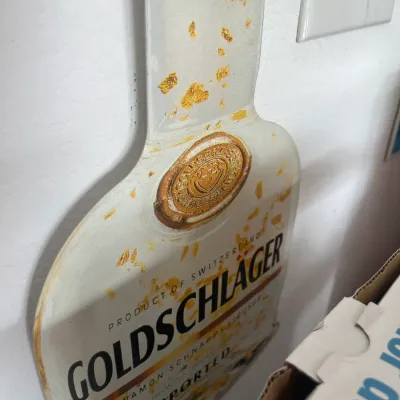 Sale Photo Thumbnail #249: Vintage Goldschläger bottle-shaped promotional wall sign featuring gold leaf graphics.