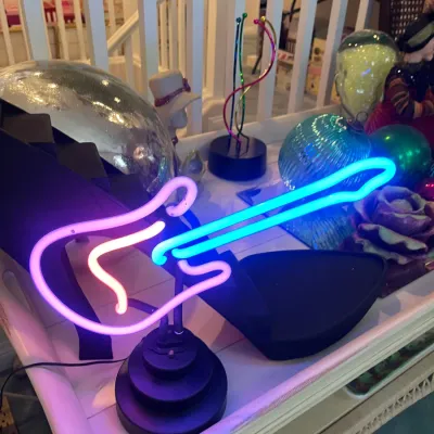 Sale Photo Thumbnail #151: Illuminated neon guitar table light featuring a purple pink body and blue neck on a tiered black base.