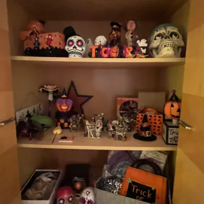 Sale Photo Thumbnail #74: Collection of Halloween and Day of the Dead decorations arranged on three wooden cabinet shelves, including sugar skulls, pumpkin figurines, and haunted house knick-knacks.
