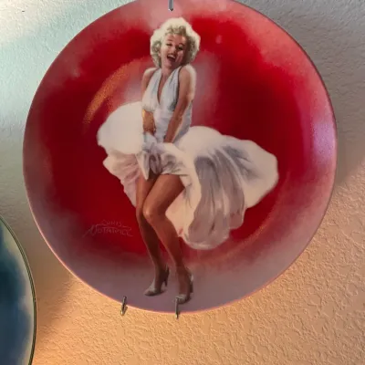 Sale Photo Thumbnail #37: Marilyn Monroe collector plate featuring art by Chris Notarile, depicting her iconic white dress pose from The Seven Year Itch against a red background.