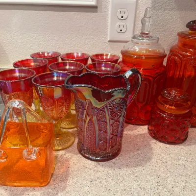 Sale Photo Thumbnail #24: Collection of vintage red and amberina glass items, featuring L.E. Smith Moon and Stars canisters, carnival glass goblets, an iridescent water pitcher, and an orange art glass basket.