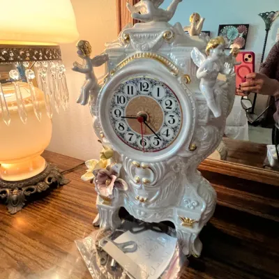 Sale Photo Thumbnail #101: Vintage white porcelain mantel clock adorned with gold accents, cherubs, and applied floral details, accompanied by a key.