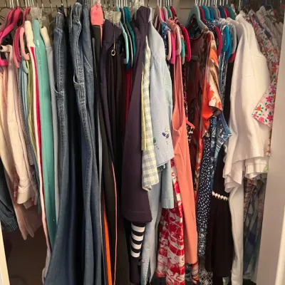 Sale Photo Thumbnail #232: Closet rod filled with various women's clothing, including denim jeans, shirts, dresses, and casual tops hanging on colorful hangers.