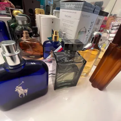 Sale Photo Thumbnail #128: Collection of men's and women's fragrances, including Ralph Lauren Polo, Avon Mesmerize, and a SpaMist aromatherapy diffuser box on a bathroom counter.